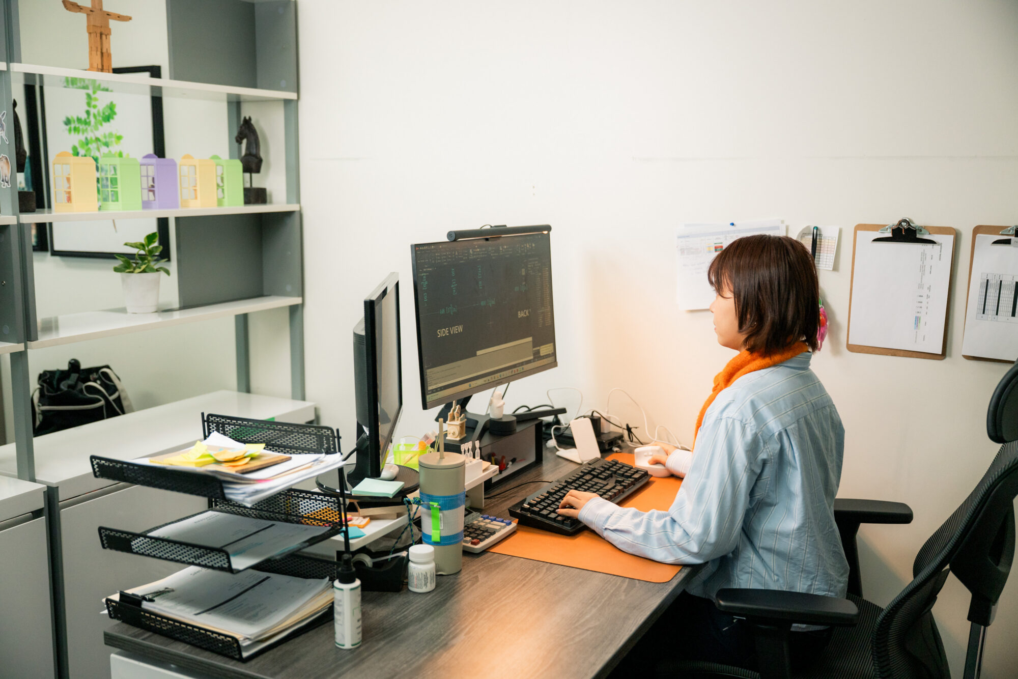 A hospitality designer in an office sitting at a desk and reviewing architectural plans for hotel furniture, casegoods, and seating specifications on a computer screen to estimate costs and lead times.